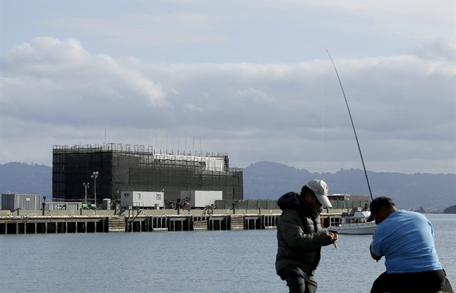 In this Tuesday, Oct. 29, 2013, file photo, two men fish in the water in front of a Google barge on Treasure Island in San Francisco.
