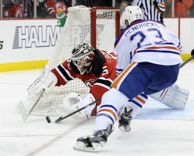 New Jersey Devils goaltender Cory Schneider, left, dives to cover the puck as Edmonton Oilers' Matt Hendricks (23) attempts to get a stick on it during the first period of an NHL hockey game on Friday, Feb. 7, 2014, in Newark, N.J.