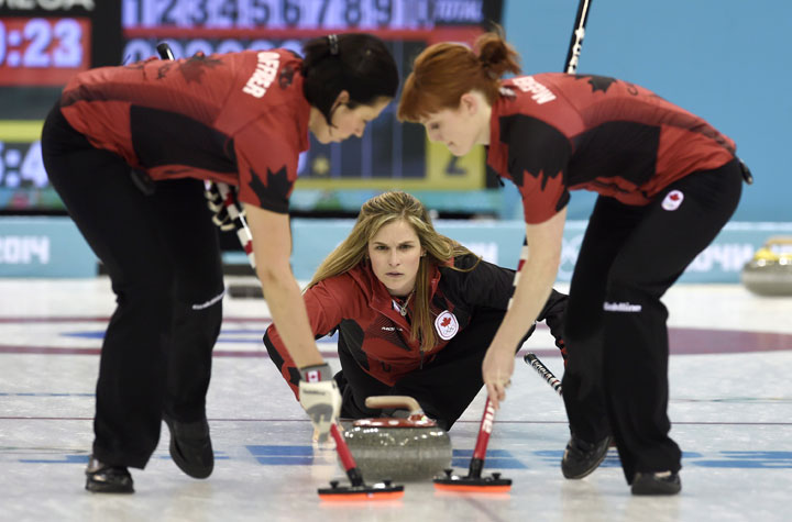 Canadian skip Jennifer Jones slides along the ice as Jill Officer (left) and Dawn McEwen sweep a rock during round robin competition against Team Russia at the Sochi Winter Olympics Sunday February 16, 2014 in Sochi, Russia. 