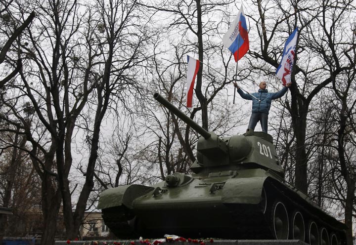 A Pro-Russian demonstrator waves Russian and Crimea flags from an old Soviet Army tank during a protest in front of a local government building in Simferopol, Crimea, Ukraine, Thursday, Feb. 27, 2014. Russian military units were blocking an airport in the Black Sea port of Sevastopol in Crimea near the Russian naval base while unidentified men were patrolling another airport serving the regional capital, Ukraine's new interior minister said Friday. 