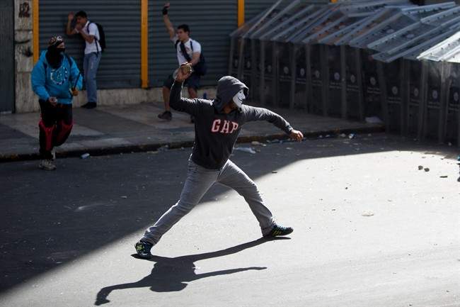 Demonstrators throw rocks at riot police during clashes between opposition protesters with security forces and pro-government supporters during a protest against the government in Caracas, Venezuela, Wednesday, Feb. 12, 2014.