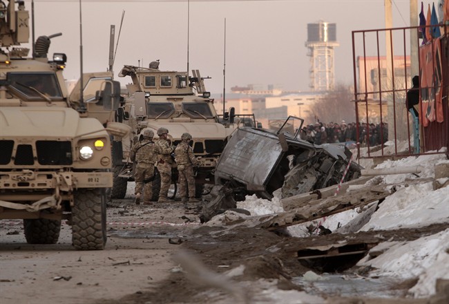 U.S. soldiers and Afghan security forces search the site where a suicide attacker rammed a car bomb into a NATO convoy killing two foreign civilian contractors, in the Afghan capital Kabul, Afghanistan, Monday, Feb. 10, 2014. 