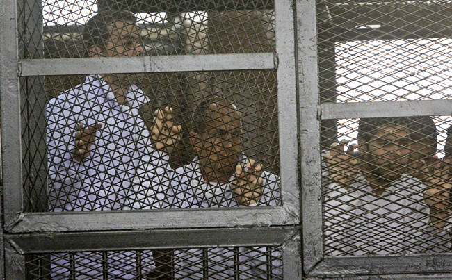 Al Jazeera producer Baher Mohamed, left, and correspondent Peter Greste, center, stand inside the defendants' cage in a courtroom during their trial on terror charges, along with several other defendants, in Cairo Egypt, Wednesday, March 5, 2014.
