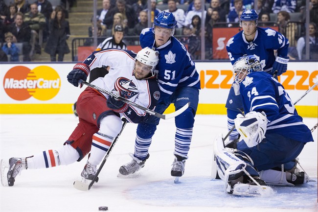 Columbus Blue Jackets goalscorer Artem Anisimov (left) and Toronto Maple Leafs' Jake Gardiner (centre) scramble for a loose puck as Leafs' goaltender James Reimer (right) looks on during third period NHL hockey action in Toronto on Monday March 3, 2014. THE CANADIAN PRESS/Chris Young.