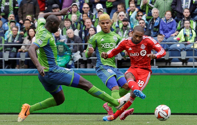 Toronto FC's Jermain Defoe, right, kicks a goal ahead of the defense of Seattle Sounders' Djimi Traore, left, and DeAndre Yedlin, center, in the first half of an MLS soccer match on Saturday, March 15, 2014, in Seattle. (AP Photo/Ted S. Warren).