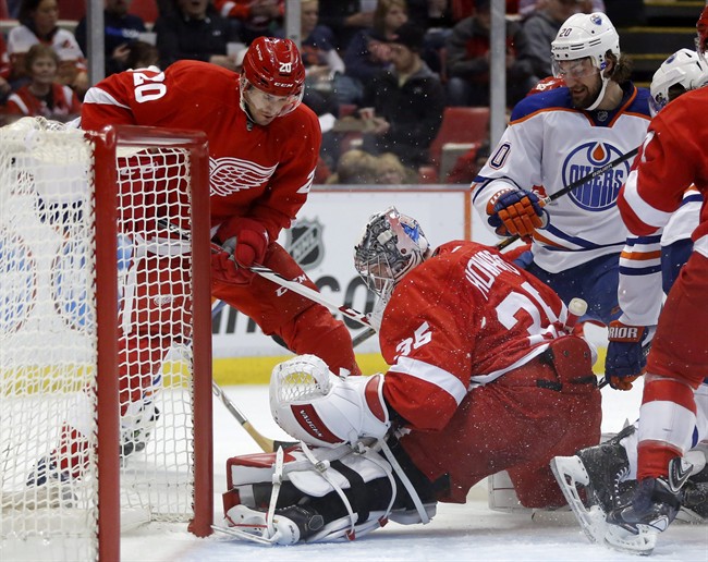 Detroit Red Wings goalie Jimmy Howard (35) stops a shot during a scrum at the net against Edmonton Oilers' Luke Gazdic, right, as Detroit Red Wings' Drew Miller, left, helps defend during the first period of an NHL hockey game Friday, March 14, 2014, in Detroit.