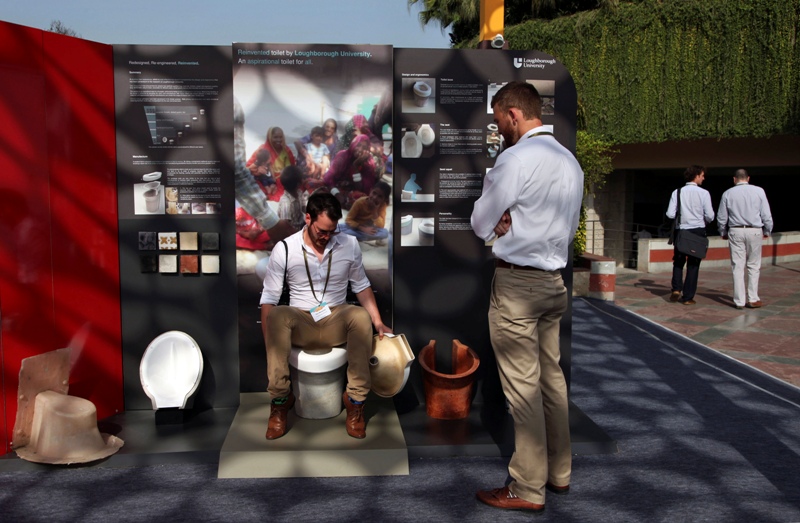 In this Friday, March 21, 2014 photo, an exhibitor from Loughborough University demonstrates the use of a toilet during Reinvent The Toilet Fair in New Delhi, India. Scientists who accepted the Bill & Melinda Gates Foundation’s challenge to reinvent the toilet showcased their inventions in the Indian capital Saturday. (AP Photo/Tsering Topgyal).
