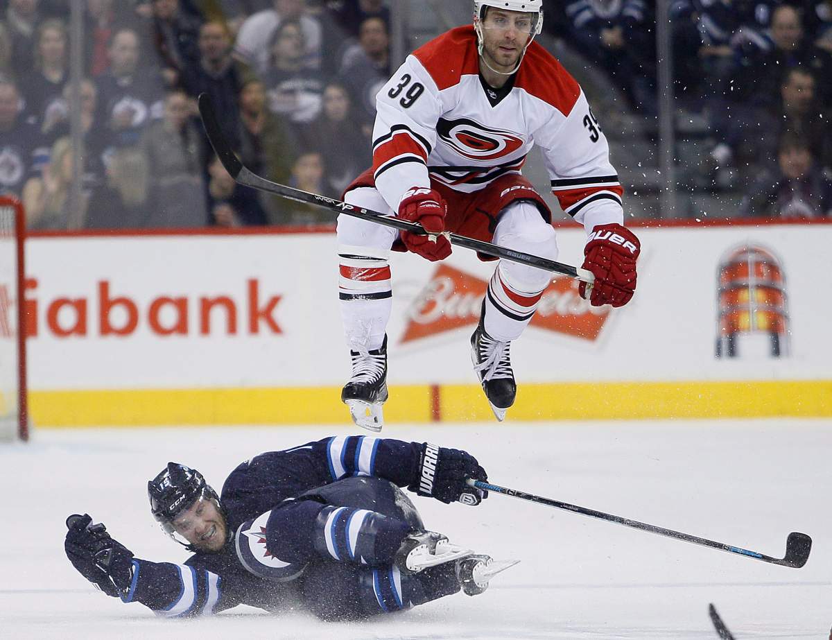 Carolina Hurricanes' Patrick Dwyer (39) leaps over Winnipeg Jets' Matt Halischuk (15) during second period NHL action in Winnipeg on Saturday, March 22, 2014. 