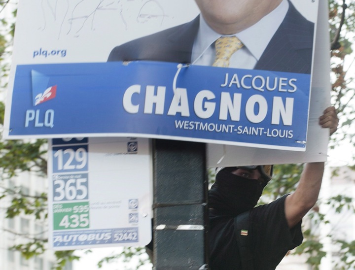 A protester dressed in black tears down an election campaign poster during a protest in Montreal, Wednesday, August 22, 2012.