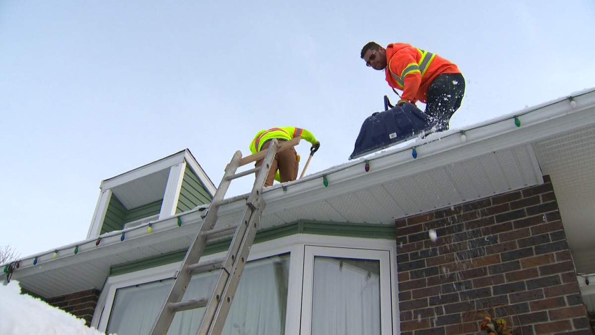In this file photo, a crew clears a roof of snow.