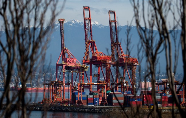 A worker drives past cargo containers stacked beneath cranes at Port Metro Vancouver in Vancouver, B.C., .