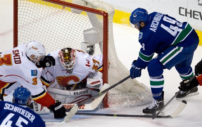 Vancouver Canucks' Darren Archibald, right, digs for the puck and eventually scores against Calgary Flames' goalie Joni Ortio, of Finland, during second period NHL hockey action in Vancouver, B.C., on Saturday March 8, 2014.