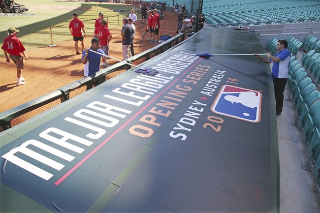 Workers clean the top of the Los Angeles Dodgers' dugout as they preparefor the Major League Baseball opening game between the Dodgers and the Arizona Diamondbacks at the Sydney Cricket ground in Sydney, Saturday, March 22, 2014. (AP Photo/Rick Rycroft).
