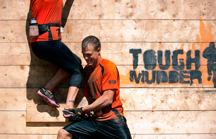 One participant helps another over the Berlin Wall obstacle at a Tuff Mudder event.