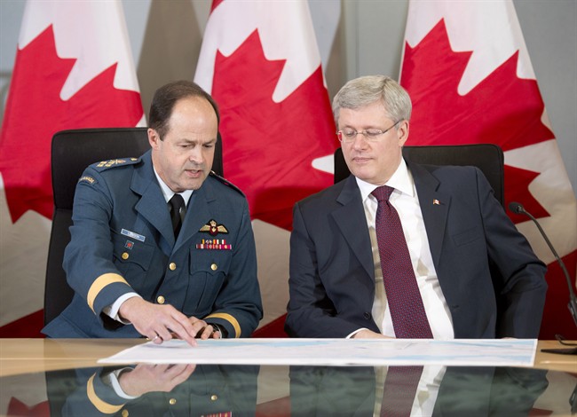 Canadian Prime Minister Stephen Harper looks over a map with the Chief of Defence Staff General Thomas Lawson before announcing Canada will send six CF-18 fighter jets to the eastern Europe as part of a NATO mission during a press conference in Ottawa on Thursday, April 17, 2014. THE CANADIAN PRESS/Adrian Wyld.