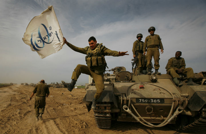 An Israeli soldier jumps off an armored vehicle carrying a flag of Israel’s 60th anniversary as he celebrates with his unit their return from the Gaza Strip on the Israeli side of the border on Jan. 16, 2009.