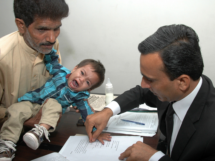This photograph taken on April 3, 2014 shows a Pakistani lawyer taking the thumb impression from nine-month-old toddler Mohammad Musa on a bail bond in Lahore. 