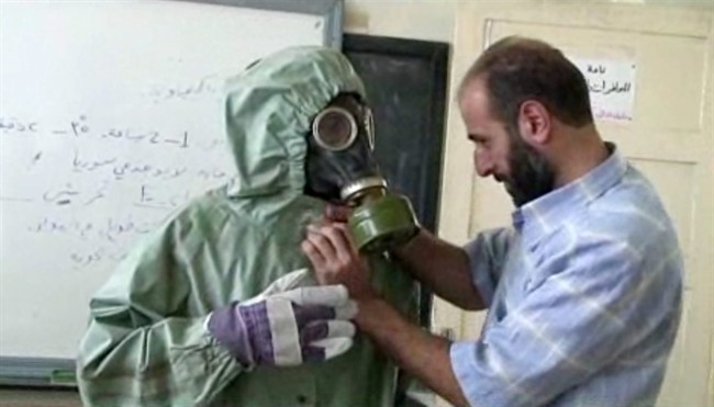 This file image made from an AP video posted on Wednesday, Sept. 18, 2013 shows a volunteer adjusting a gas mask and protective suit on a student during a classroom session a on how to respond to a chemical weapons attack in Aleppo, Syria.