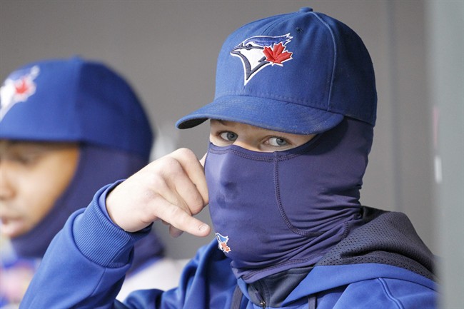 Toronto Blue Jays third baseman Brett Lawrie imitates talking on a phone as he sits bundled up in the dugout during the first inning of the MLB American League baseball game against the Minnesota Twins where the temperature was 36 degrees at game time in Minneapolis, Tuesday, April 15, 2014. (AP Photo/Ann Heisenfelt).
