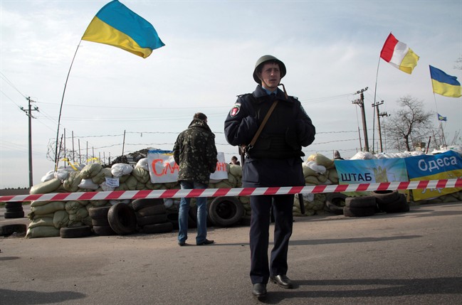 A Ukrainian police officer stands guard at a checkpoint, with Ukrainian flags, that was attacked by unknown men outside the Black Sea port of Odessa, Ukraine, Friday, April 25, 2014. 