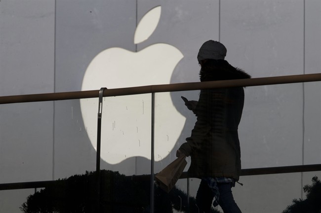 In this Dec. 23, 2013 file photo, a woman using a phone walks past Apple's logo near its retail outlet in Beijing. Apple reports quarterly earnings on Wednesday, April 23, 2014.
