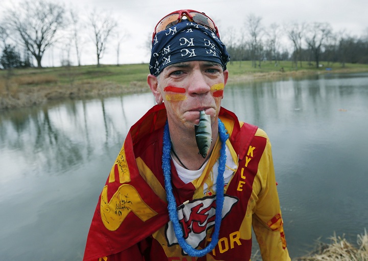 Kansas City Chiefs fan Ty Rowton, known as XFactor, exits the water with a toy fish in his mouth after takeing a Plunge for Landon in a farm pond near Bonner Springs, Kan., Friday, April 4, 2014.