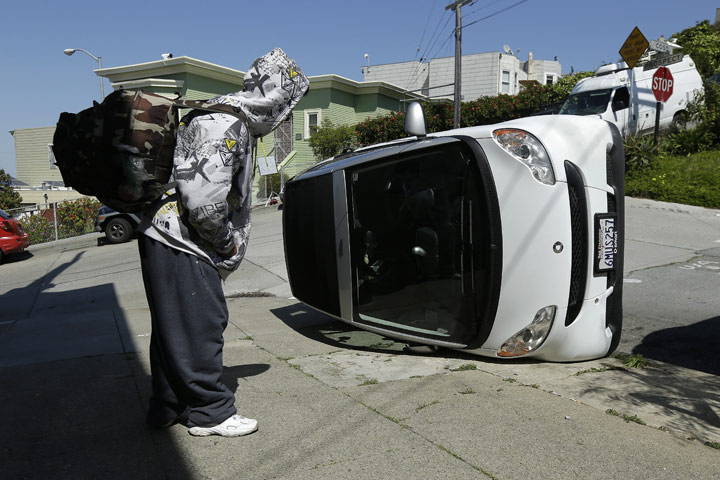 A man looks at a tipped over Smart car on the corner of Prospect and Coso Avenues in San Francisco, Monday, April 7, 2014. 