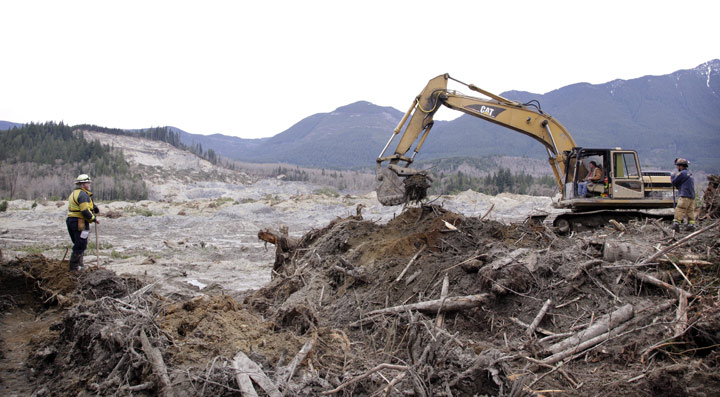 Workers move debris at the scene of a deadly mudslide, torn off from the hill at upper left almost two weeks earlier, Thursday, April 3, 2014, in Oso, .
