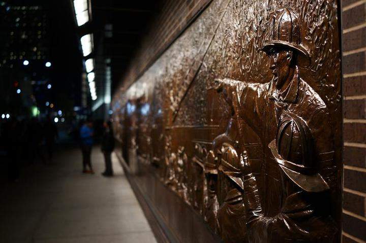 People walk by a memorial to firefighters killed on September 11 near the grounds at the Ground Zero memorial site after authorities recently took down gates and opened the plaza to the public on May 19, 2014 in New York City.