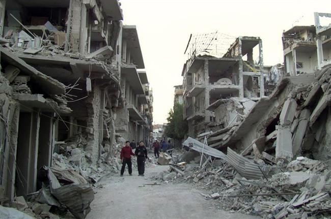 This file photo released on Thursday Nov. 29, 2012 by the anti-government activist group Homs City Union of The Syrian Revolution, which has been authenticated based on its contents and other AP reporting, shows Syrian citizens walking in a destroyed street that was attacked by Syrian forces warplanes, at Abu al-Hol street in Homs province, Syria. (AP Photo/Homs City Union of The Syrian Revolution, File).