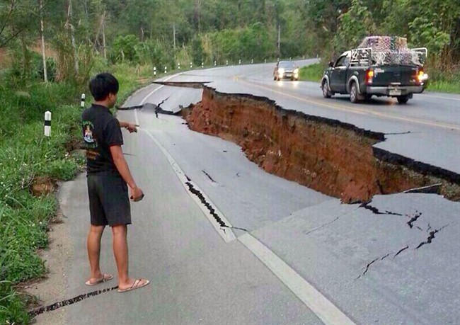 A man points a big crack on a damaged road following a strong earthquake in Phan district of Chiang Rai province, northern Thailand, Monday, May 5, 2014. A strong earthquake shook northern Thailand and Myanmar Monday evening, and some light damage was reported.