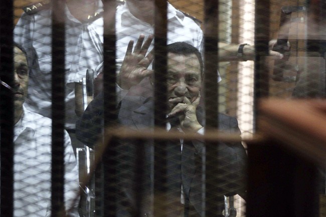 Ousted Egyptian President Hosni Mubarak, sitting in a defendants cage, waves during a court hearing as his son Gamal, left, in Cairo, Egypt, Wednesday, May 21, 2014. 