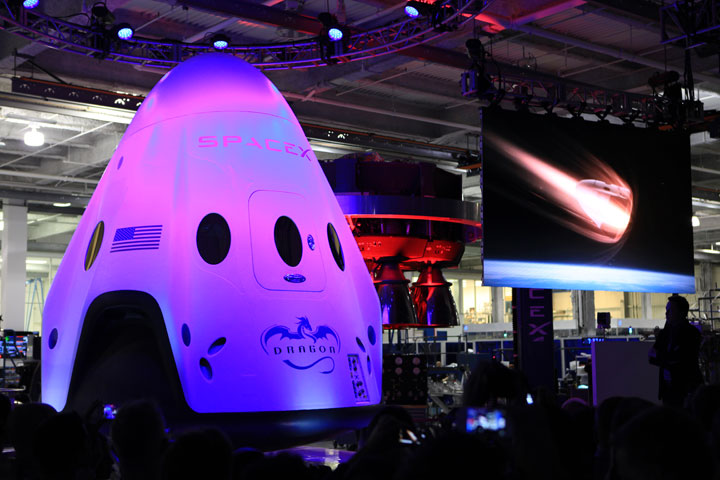 An artist concept video of the Dragon V2 re-entering Earth's atmosphere plays alongside the newly unveiled spacecraft May 29, 2014, at SpaceX headquarters in Hawthorne, California.