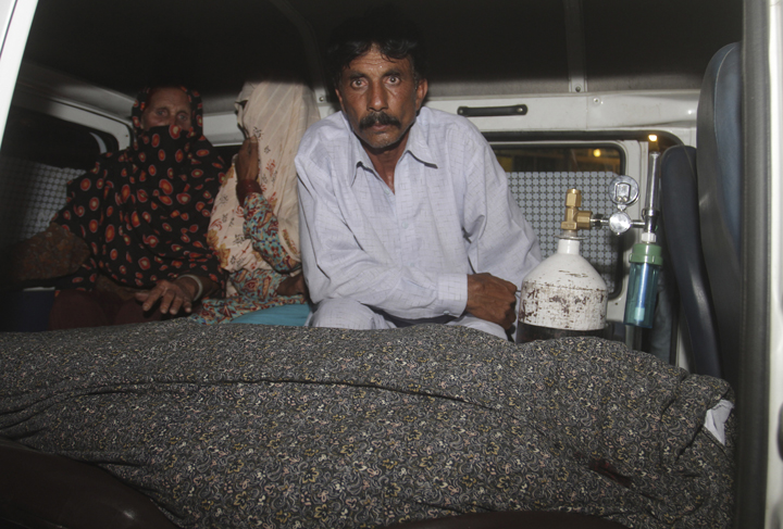 Mohammad Iqbal, right, husband of Farzana Parveen, 25, sits in an ambulance next to the body of his pregnant wife who was stoned to death by her own family, in Lahore, Pakistan, Tuesday, May 27, 2014.