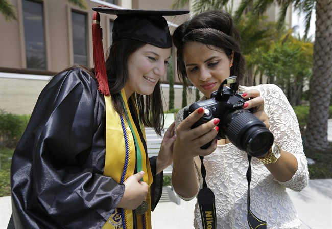 In this April 29, 2014 photo, University of South Florida graduating seniors Kyra Ciotti, 22, of Tampa, Fla., left, and Rita Sibaja, 24, of Winter Haven, Fla., look at photos that Rita took of Kyra in her cap and gown Tuesday, April 29, 2014, in Tampa, Fla. 