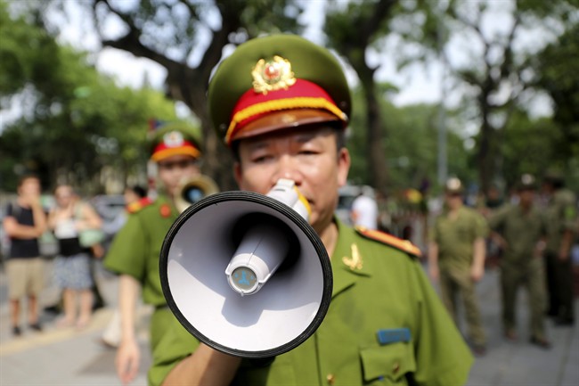 A Vietnamese police officer uses a speaker to order pedestrians including journalists to leave a closed area near the Chinese Embassy in Hanoi, Vietnam on Sunday, May 18, 2014. 