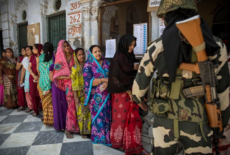 Indian women wait in line to vote as a border police officer stands guard at a polling station on May 12, 2014 in Varanasi, India. Indians voted in the ninth and final phase of elections Monday. Counting will be on May 16. (Photo by Kevin Frayer/Getty Images).