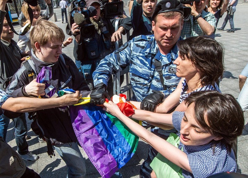 A man (L) takes away a rainbow flag as a policeman detain gay rights activists during their protest in central Moscow on May 31, 2014. AFP PHOTO / DMITRY SEREBRYAKOV.