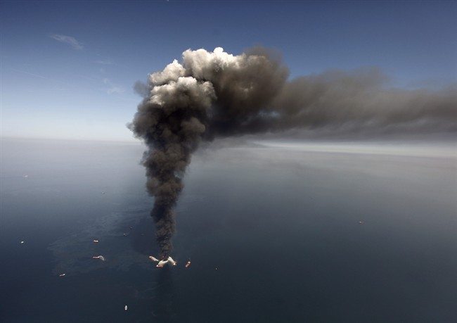 FILE - In this Wednesday, April 21, 2010 file photo, oil can be seen in the Gulf of Mexico, more than 50 miles southeast of Venice on Louisiana's tip, as a large plume of smoke rises from fires on BP's Deepwater Horizon offshore oil rig.
