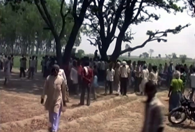 In this Wednesday, May 28, 2014 image taken from video, a crowd gathers near where two teenage sisters were found hanging from a mango tree in Katra village in Uttar Pradesh state, in northern India. 
