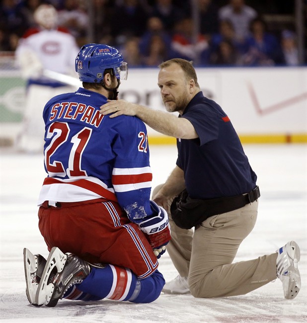 In this May 22, 2014 photo, a staff member examines New York Rangers center Derek Stepan (21) after Stepan took a hit from Montreal Canadiens forward Brandon Prust during the first period of Game 3 of the NHL hockey Stanley Cup playoffs Eastern Conference finals in New York. (AP Photo/Kathy Willens).