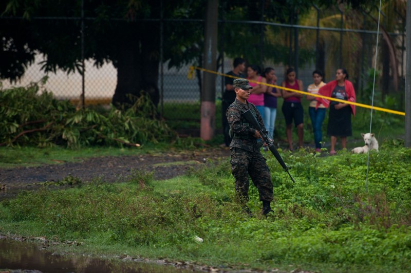 A soldier stands guard as police investigators inspect the crime scene following a targeted attack on a bus in the town of San Luis Talpa, 38 km south of San Salvador, on May 23, 2014. Six people were shot dead and four wounded in a suspected gang attack on a bus near El Salvador's international airport on Friday, police said. AFP PHOTO/Jose CABEZAS.