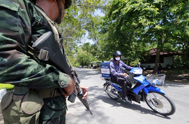 A Thai soldier looks at a motorcyclist riding past while providing security near the pro-government demonstration site on the outskirts of Bangkok, Thailand Wednesday, May 21, 2014. 