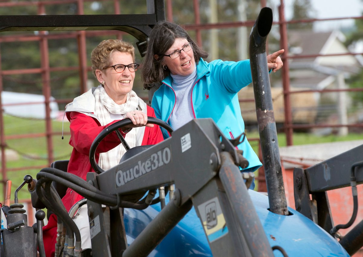 Ontario Premier Kathleen Wynne drives a tractor with instruction from farmer Sandra Vos (right) at a campaign event in Paris, Ontario on Tuesday May 20.