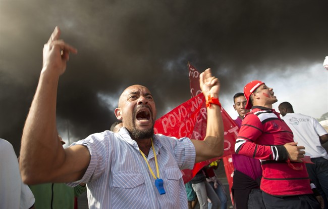 Members of the Homeless Workers Movement protest against the money spent on the World Cup near Itaquerao stadium which will host the international soccer tournament's first match in Sao Paulo, Brazil, Thursday, May 15, 2014. Brazilians are angry at the billions spent to host the World Cup, much of it on 12 ornate football stadiums, one-third of which critics say will see little use after the big event. The smoke behind comes from burning tires. (AP Photo/Andre Penner)
