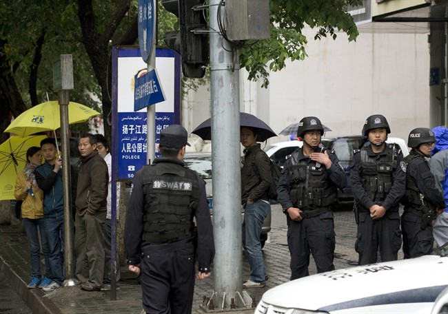 People watch armed policemen standing guard near the site of an explosion in Urumqi, northwest China's Xinjiang region in May 2014. Assailants in two SUVs had plowed through shoppers while setting off explosives on a busy street market, killing over two dozen people and injuring more than 90.