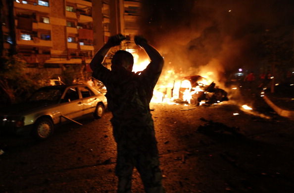 A security officer gestures as fire takes over cars at the site of a car bomb attack in the mainly Shiite populated Shayyah neighborhood of a Beirut southern suburb, early on June 24, 2014. The explosion, likely carried out by a suicide attacker, happened around midnight local time on June 24 near an army checkpoint and a cafe where football fans were watching the World Cup.   AFP PHOTO/ANWAR AMRO        (Photo credit should read ANWAR AMRO/AFP/Getty Images).