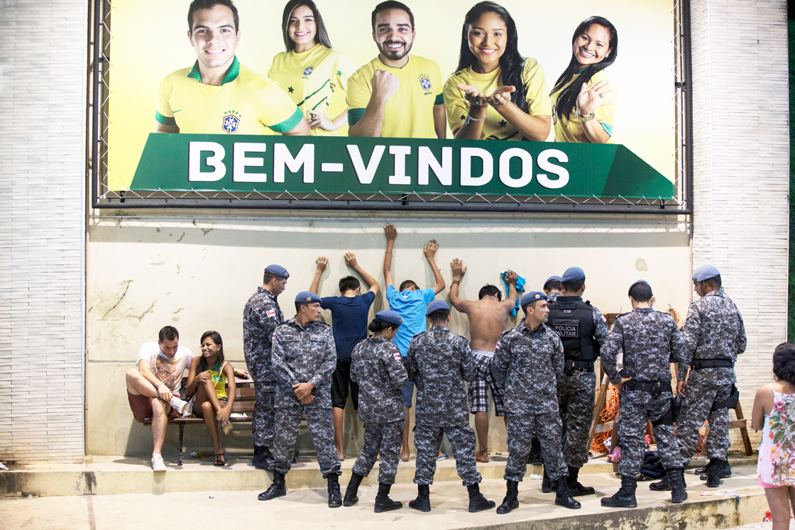 MANAUS, BRAZIL - JUNE 17: Military police search young men outside the Fan Fest area in Porta Negro, under a large sign that reads: 'Welcome,' June 17, 2014 in Manaus, Brazil. Brazil, the host nation of the 2014 FIFA World Cup, played their second group match against Mexico in Fortaleza today which ended 0-0. (Photo by Oli Scarff/Getty Images)