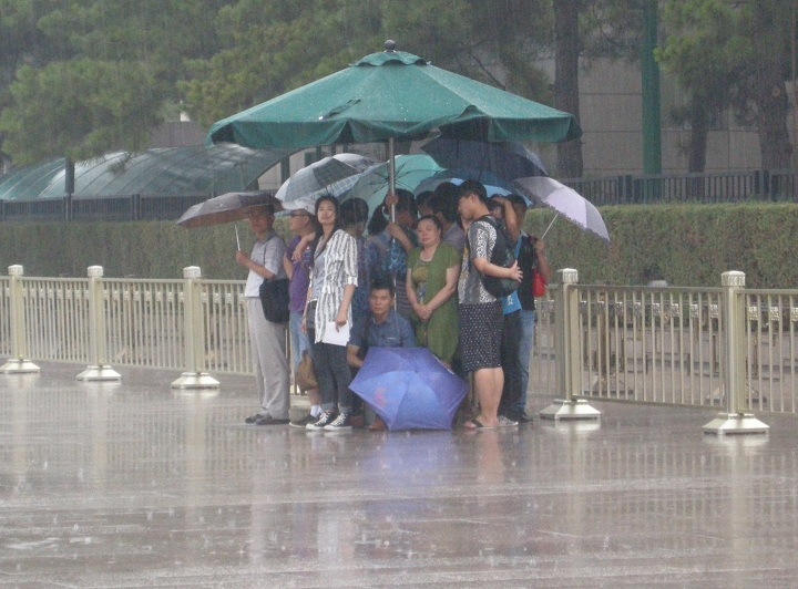 People take shelter from rain under a giant umbrella on June 17, 2014 in Beijing, China.
