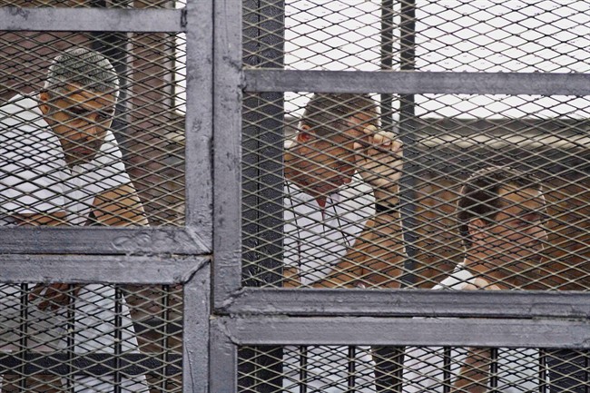 Mohammed Fahmy, (left to right) Canadian-Egyptian acting bureau chief of Al-Jazeera, Australian correspondent Peter Greste, and Egyptian producer Baher Mohamed appear in a defendant's cage along with several other defendants during their trial on terror charges at a courtroom in Cairo in this Thursday, May 15, 2014 file photo.